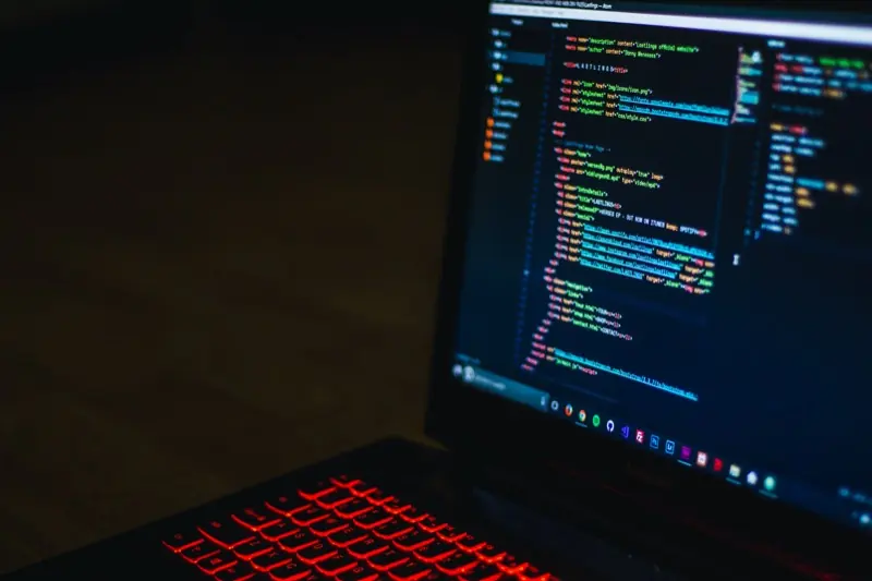 Aufgeklappter Laptop mit farbigem Quelltext auf dunklem Bildschirm