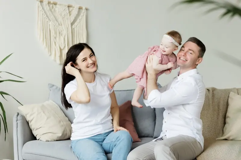Eltern halten lachend ihr Kleinkind auf dem Sofa hoch