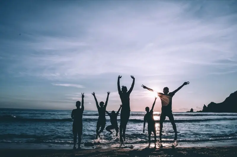 Sechs Menschen springen bei Sonnenuntergang am Strand in die Luft